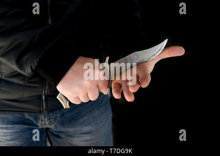 Crime, a man in a leather jacket and jeans in a dark room defiantly cuts his hand with a knife Stock Photo