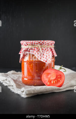 Homemade adjika with tomatoes in jar on black background. Close-up Stock Photo