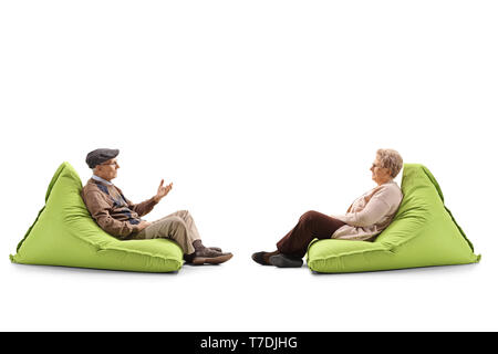 Full length profile shot of an elderly couple sitting on a bean bag armchairs and talking isolated on white background Stock Photo