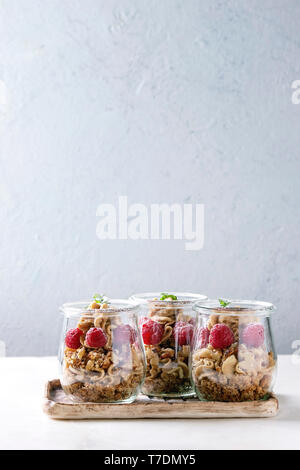 Layered dessert in jars. Biscuit, coffee cream, nuts, raspberries, fresh mint. Served on ceramic tray over white marble table. Stock Photo