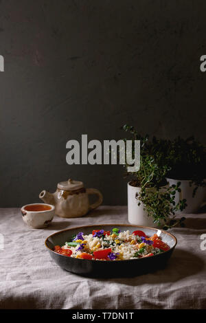 Couscous salad with parboiled vegetables baby carrots, green beans, sweet corn, spinach in ceramic plate with tomatoes, sesame and edible flowers, tea Stock Photo