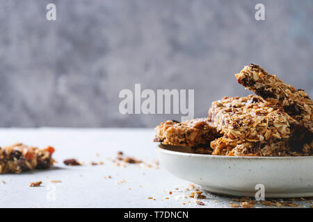 Homemade energy oats granola bars with dried fruits and nuts whole and broken in ceramic plate on grey table. Healthy snack. Stock Photo