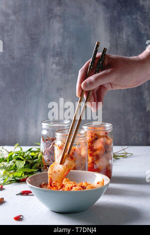 Korean traditional fermented appetizer kimchi cabbage and radish salad, fish snack served in glass jars with Vietnamese oregano and chili peppers over Stock Photo