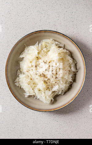 White sauerkraut chopped cabbage pickled in brine with cumin in ceramic plate over grey spotted background. Flat lay, space Stock Photo