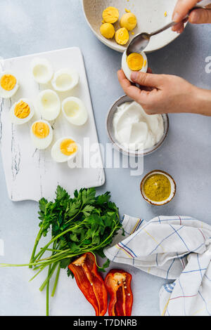 Woman preparing deviled eggs with mustard and greek yogurt on a grey background. Stock Photo