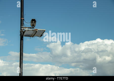 CCTV protected by barbed wire on street lamp pole, above clouds. Stock Photo