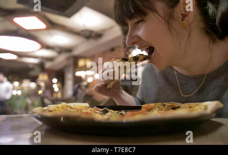 Young woman eating a slice of pizza sitting in a cafe Stock Photo