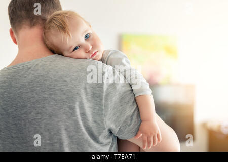 Close-up portrait of cute adorable blond caucasian toddler boy on fathers shoulder indoors. Sweet little child feeling safety on daddys hand. Responsi Stock Photo
