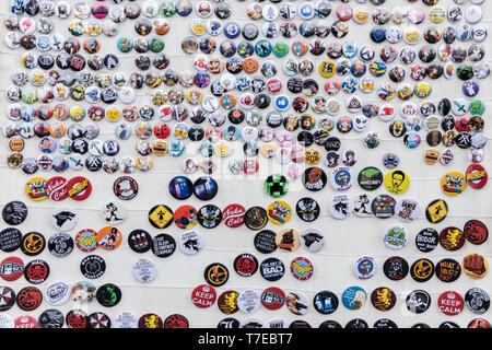 Wall of badges depicting cartoon and SciFi characters and slogans in english and Spanish Stock Photo