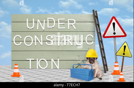 cute repairman pug puppy dog with yellow safety helmet, sitting down next to wooden board sign, with text under construction Stock Photo