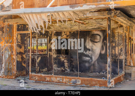 A building gutted by wildfire has a large face painted on an inside wall, looking out to the street, in the town of Paradise, California the site of t Stock Photo
