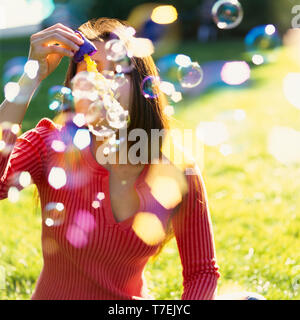 Beautiful, happy, healthy young brunette woman having fun blowing bubblies outdoors on a sunny summer day Stock Photo