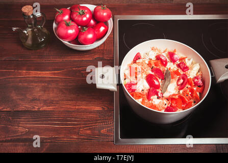 Stewed vegetables, tomatoes, carrots, cabbage, peppers in a saucepan on an electric stove and a wooden table. Stock Photo