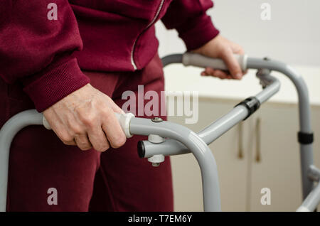 Senior woman standing and walking with her hands on the handles of a walker. Rehabilitation and healthcare concept. Stock Photo