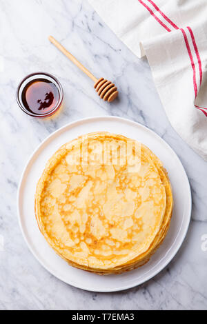 Crepes, blini, thin pancakes with honey on a white plate. Marble background. Top view. Stock Photo