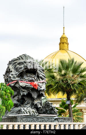 close up big black lion statue with red scarf sitting front of building., Laos. Stock Photo