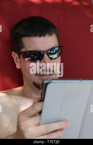 Portrait of a man with sunglasses and a beard looking at his tablet Stock Photo