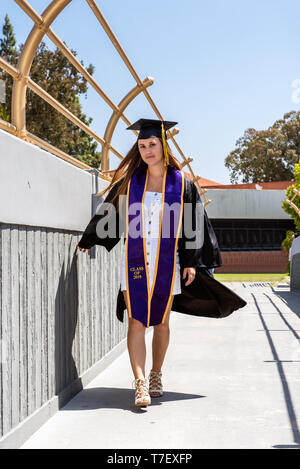 Beautiful young female student walking with attitude and confidence while dragging hand along student walkway of campus. Stock Photo