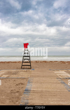 Red danger flag flying before a storm, on a windy and cloudy day on the beach at Alicante in spain Stock Photo