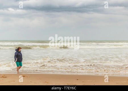 middle aged woman walking alone on a beach on a stormy day in Alicante Spain Stock Photo