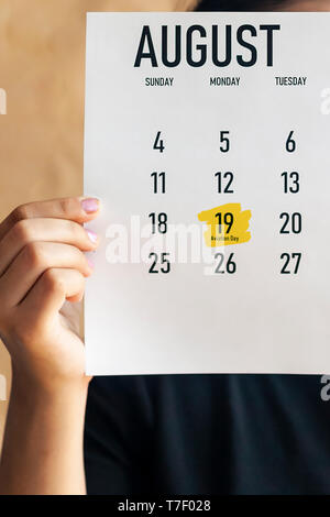 A woman holding August calendar with marked National Aviation Day. 19 August marked with a yellow marker at 2019 calendar. Stock Photo