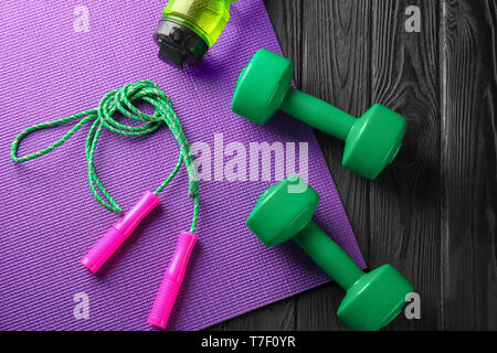 Yoga mat with jump rope and  dumbbells on wooden background Stock Photo