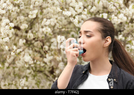 Young woman using inhaler near blooming tree. Allergy concept Stock Photo