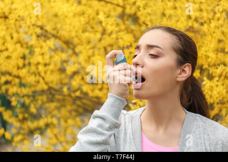 Young woman using inhaler near blooming tree. Allergy concept Stock Photo