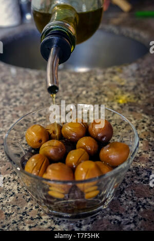 Pouring olive oil on the green olives from the glass bottle close up view Stock Photo