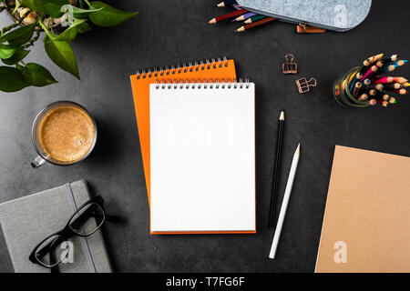 Design concept - top view of copy space with orange spiral notebook, potted plant, glasses, coffee, pencil on black background for mockup Stock Photo