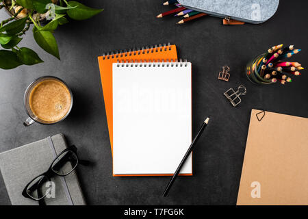 Design concept - top view of copy space with orange spiral notebook, potted plant, glasses, coffee, pencil on black background for mockup Stock Photo