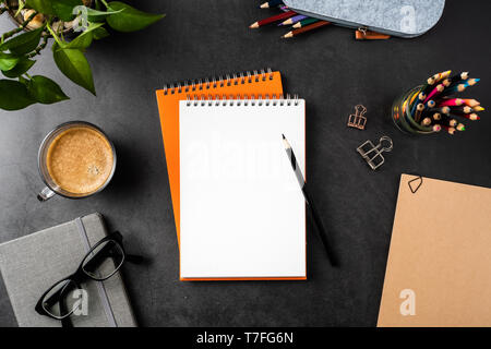 Design concept - top view of copy space with orange spiral notebook, potted plant, glasses, coffee, pencil on black background for mockup Stock Photo