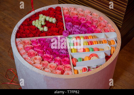 Colorful macarons cake . Paper Box with french dessert - macaroons on gray concrete table with festive decoration. Red and purple flowers Stock Photo