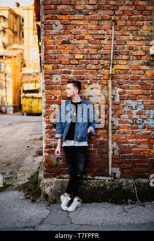 Young man in front of brick wall holding cigarette Stock Photo