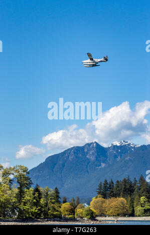 Vancouver, BC, - May 5, 2019:  Fairmont Hotel commuter plane flying West over Coal Harbour. Stanley Park and North Shore Mountains in background. Stock Photo