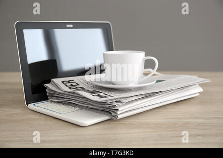 Pile of newspapers, laptop and cup of coffee on wooden table Stock Photo