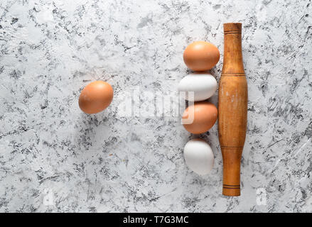 Eggs, rolling pin on white concrete surface. The cooking process, ingredients and cutlery kitchen tools. Stock Photo