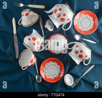 Antique set of dishes on a dark cloth tablecloth. Ceramic teapot, saucer, cup, spoon, fork, knife. Top view. Stock Photo