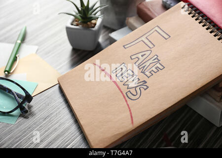 Notebook with phrase FAKE NEWS on table Stock Photo