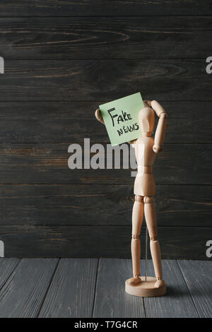 Wooden small mannequin holding sticker with phrase FAKE NEWS on table Stock Photo