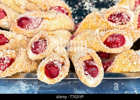 Many prepared hot dogs wrapped in a sweet bread and sprinkled with cheese laying on a metal tray. Typical cheap street food in the Philippines. Stock Photo