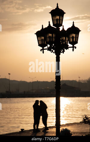 streetlight in sunset with two people taking selfie photo in front of the sea Stock Photo