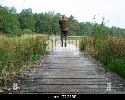 Birdwatcher (man) standing on a boardwalk in Dutch nature reserve. Looking at a bird on the lake. Concept for future, discovery, exploring and educati Stock Photo