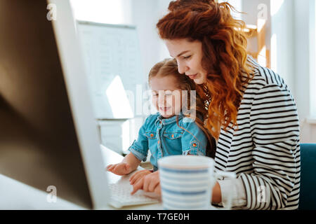 Daughter sitting on knees of mother and trying using keyboard Stock Photo