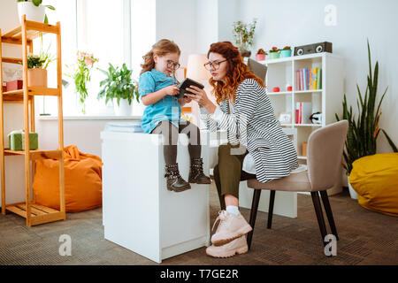 Funny daughter wearing glasses using calculator in the office of mom Stock Photo