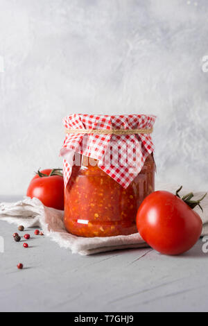 Homemade vegetable sauce adjika with tomatoes in jar on light background. Close-up. Space for text. Stock Photo