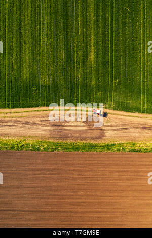 Aerial view of tractor with attached crop sprayer on countryside dirt road heading toward the field, top down view from drone pov Stock Photo