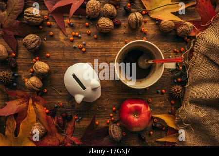 Piggy coin bank with autumn decoration arrangement on wooden table, flat lay top view retro toned Stock Photo