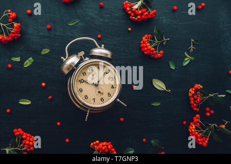 Ten after ten on alarm clock, flat lay top view minimal composition of timepiece placed on dark wooden background with retro floral arrangement Stock Photo