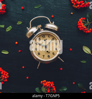 Ten after ten on alarm clock, flat lay top view minimal composition of timepiece placed on dark wooden background with retro floral arrangement Stock Photo